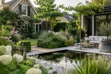 Tuin met vijver, terrasbank en cottage-huis, bloeiende struiken en omliggend groen