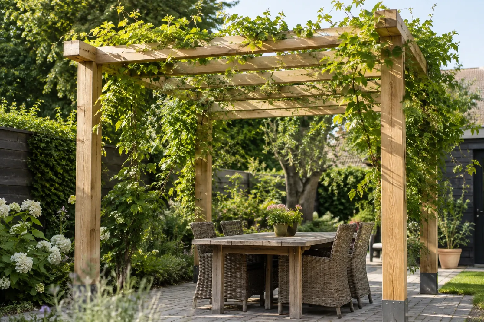 Houten pergola met klimplanten boven tuintafel en rieten stoelen in zonlicht